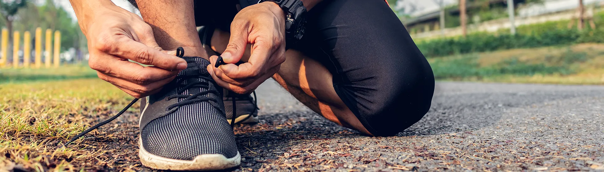 A man is kneeling down to tie his shoes before going for a run on a path.