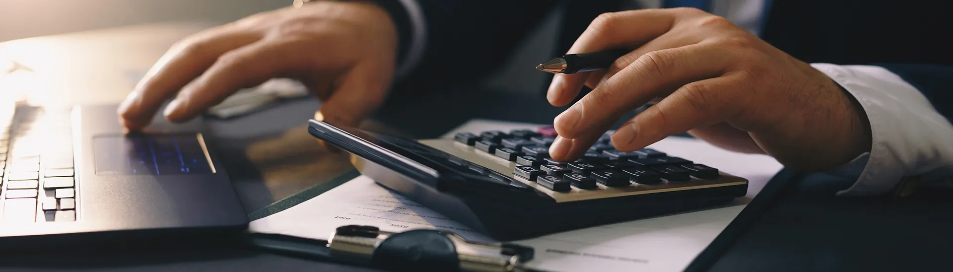 Un hombre calcula información financiera utilizando una calculadora y un ordenador portátil.