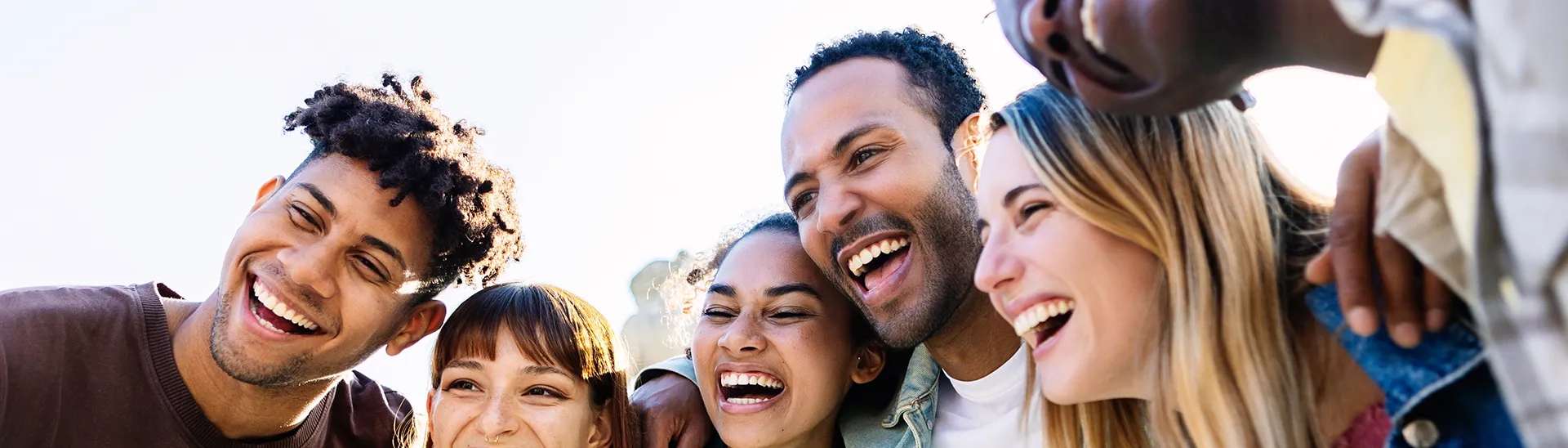 A group of different men and women smiling and laughing with their arms around each others shoulders.