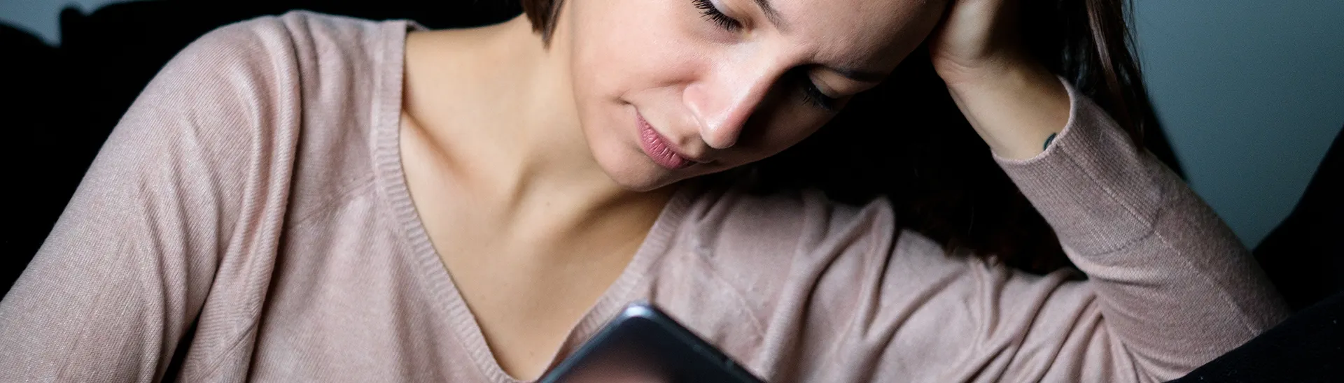 A woman looking down at her phone with her hand on her head thinking about getting help.