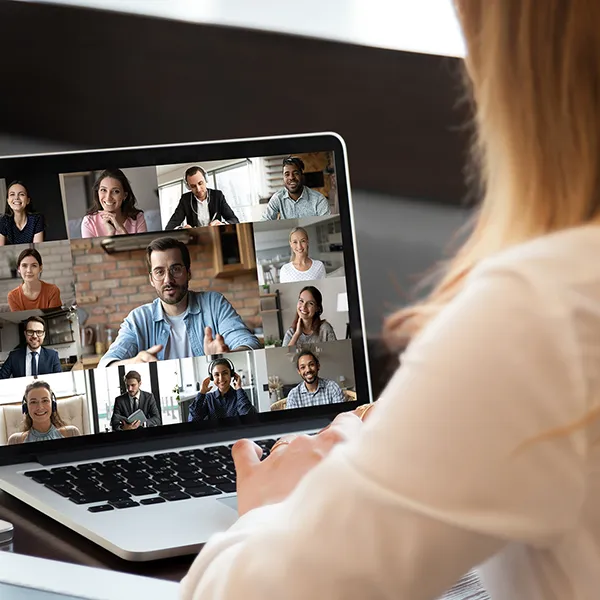 A woman sits online watching a community conversation around health care with other members on her laptop meeting together.