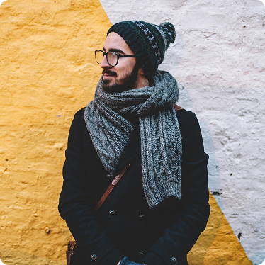 man-with-glasses-leaning-on-wall Man with glasses and scarf leaning against a concrete wall.