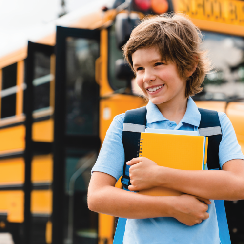 Back to school with a boy standing in front of a bus holding his notebooks.