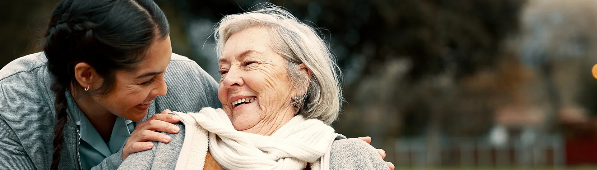 Elderly woman sharing a smile with a younger health care assistant.