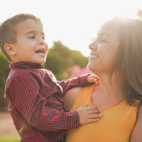 A mother and holding her son smiling together in the warm sun light.