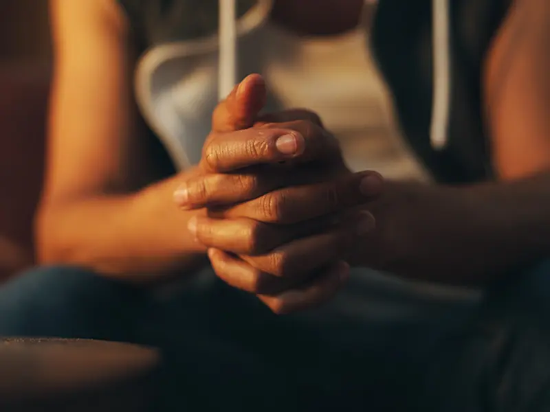 Un hombre afroamericano sentado con las manos cruzadas pidiendo ayuda.