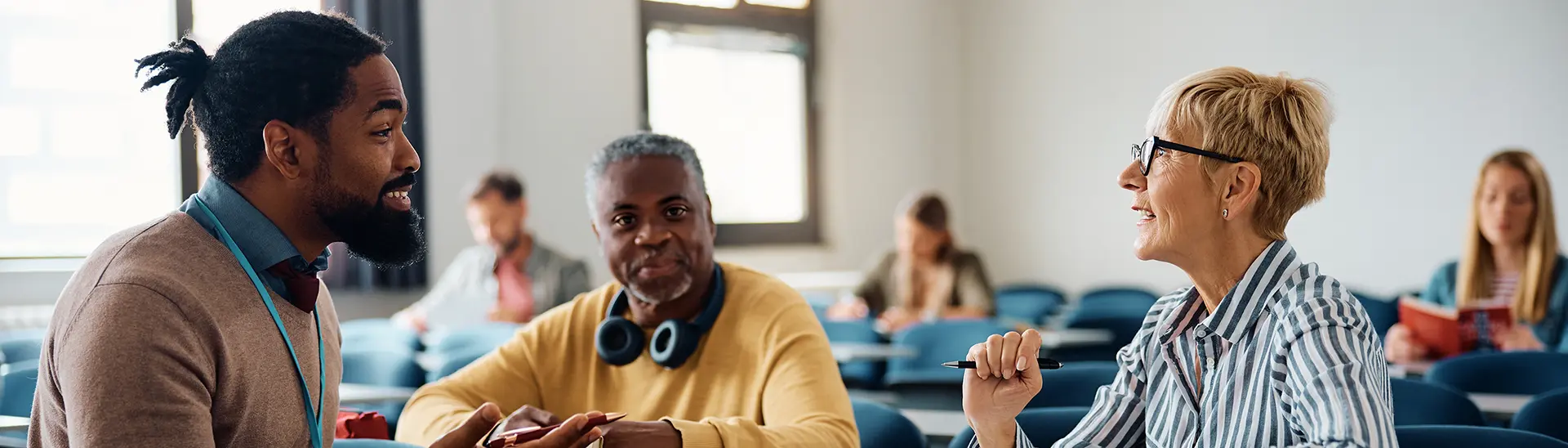 Three primary people in classroom are talking together, two men and a woman.