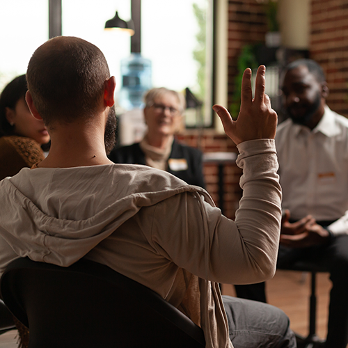 A member of an alcoholic anonymous group raises their hand to speak.